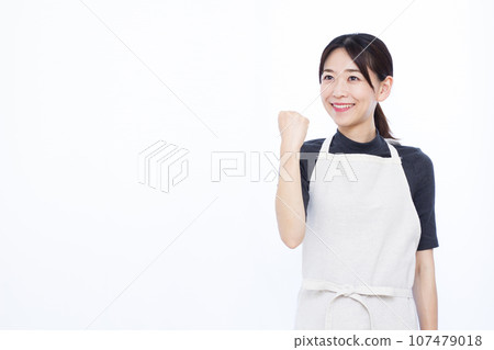 A housewife in her 30s standing in front of a white background and doing a fist pump 107479018