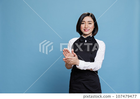 Cheerful asian waitress applauding and looking at camera with happy expression. Smiling joyful woman receptionist making applause, congratulating and celebrating success portrait 107479477