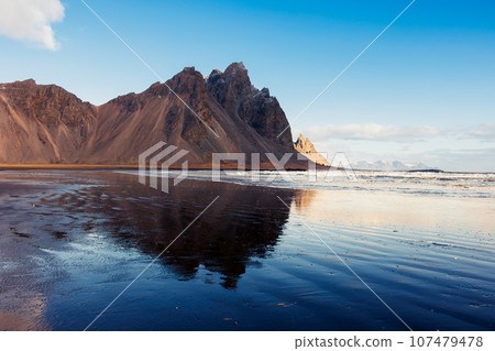 Towering alpine vestrahorn hills, icelandic fantastic environment on peninsula of Stokksnes. Overview of scandinavian nordic scenery with lovely black sand beach in frozen Iceland. Towering alpine vestrahorn hills, icelandic fantastic environment on peninsula of Stokksnes. Overview of scandinavian nordic scenery with lovely black sand beach in frozen Iceland. 107479478