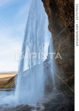 Inside arctic skgafoss waterfall with river stream frunning down off mountain edges, icelandic cascade with water flow falling. Scandinavian nature and wilderness, beautiful landscape. 107479501