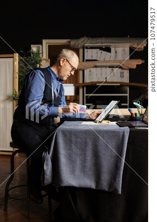 Fashion designer ready to buy sewing materials he needs for upcoming client bespoken comission after finding inspiration online. Elderly suitmaker purchasing tailoring materials with credit card 107479517