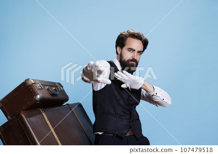 Groovy male bellhop dancing on camera, feeling happy and confident with silly dance moves in formal attire. Young professional doorman acting funky and fooling around in studio. Groovy male bellhop dancing on camera, feeling happy and confident with silly dance moves in formal attire. Young professional doorman acting funky and fooling around in studio. 107479518