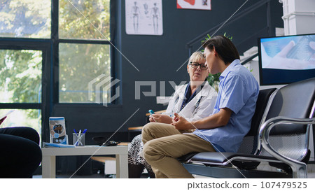 Senior doctor examining asian patient with glucometer during consultation, measuring insulin and glucose level from blood sample. Young adult doing diabetic control in hospital waiting area 107479525
