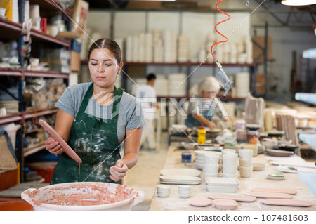 Girl potter painting plates in workshop 107481603