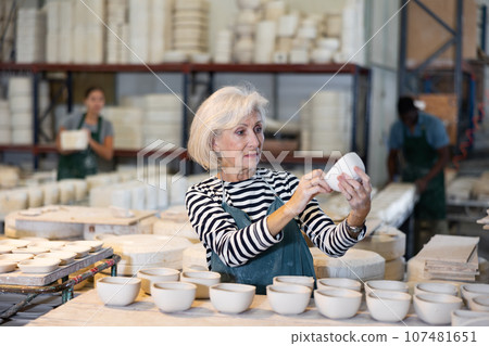 Mature woman ceramist arranging new bowls in workshop Mature woman ceramist arranging new bowls in workshop 107481651