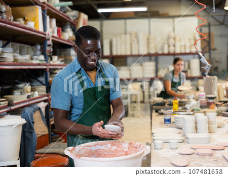 Cheerful man potter painting plates in workshop 107481658