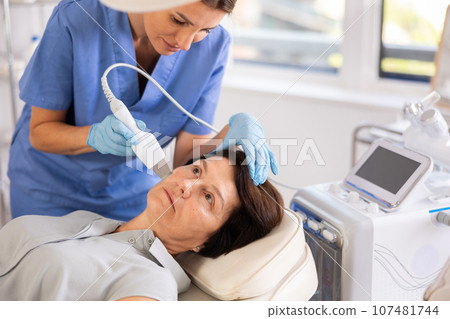 Mature woman undergoing hardware cosmetic facial treatment using ultrasonic shovel 107481744