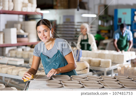 Positive girl ceramist polishing new clay plates 107481753