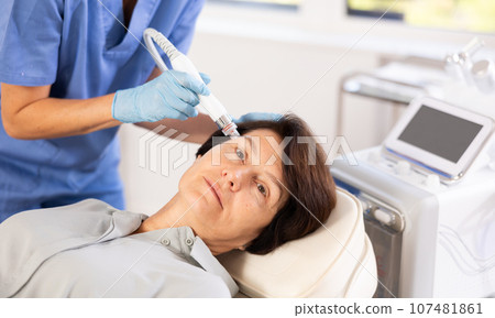 Mature woman receiving facial procedure with hydrogen and oxygen ions attachment 107481861