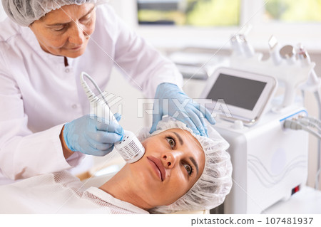 Young woman experiencing facial cryotherapy procedure using ice hammer Young woman experiencing facial cryotherapy procedure using ice hammer 107481937