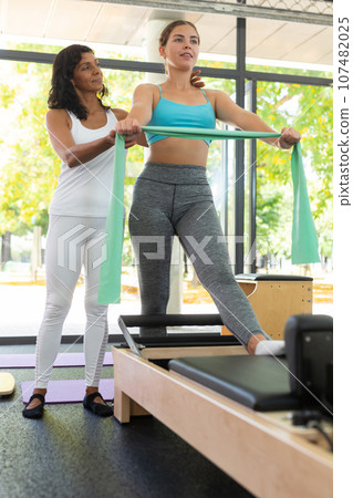 Experienced Latina female instructor helping positive girl during training with resistance bands 107482025