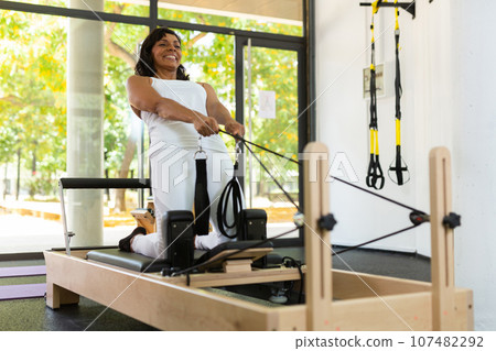 Young Latina practicing pilates stretching exercises on reformer 107482292