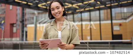 City girl standing with tablet on street, using application, smiling at camera 107482514