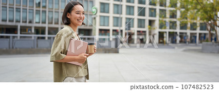 Stylish city girl with tablet, walking on street and drinking takeaway coffee, going to university or work Stylish city girl with tablet, walking on street and drinking takeaway coffee, going to university or work 107482523
