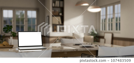A white-screen laptop mockup on a dining table in a modern spacious living room. Home workspace 107483509