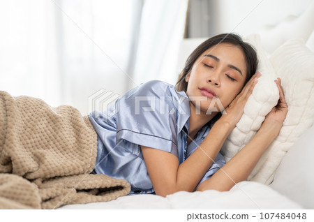 A relaxed and carefree Asian woman in pajamas is sleeping in her comfy bed in her bedroom A relaxed and carefree Asian woman in pajamas is sleeping in her comfy bed in her bedroom 107484048