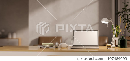 A wooden desk in a minimalist home office with a white-screen laptop mockup and accessories. 107484093