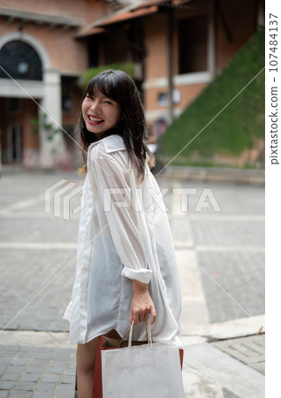 A pretty Asian woman is carrying her shopping bags and enjoying her shopping day in the city. 107484137