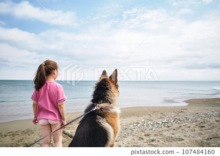 A girl in a pink T-shirt and a dog look at the sea. A girl in a pink T-shirt and a dog look at the sea. 107484160
