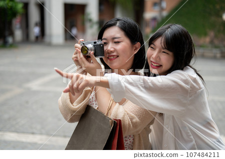 Two happy Asian female friends are strolling around the city, using a film camera to take a picture. Two happy Asian female friends are strolling around the city, using a film camera to take a picture. 107484211