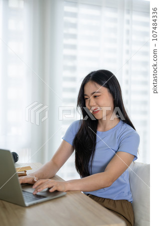 A beautiful Asian woman in casual clothes using her laptop, working on her laptop in her room. 107484336