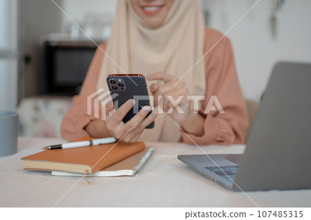 Close-up image of a Muslim woman is using her smartphone at a table in the kitchen 107485315