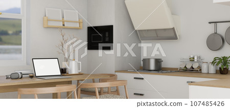 A laptop mockup on a wooden dining table in a minimalist white kitchen A laptop mockup on a wooden dining table in a minimalist white kitchen 107485426
