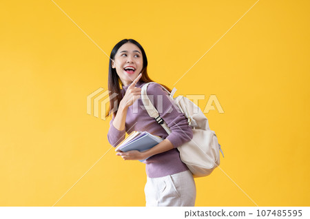 A cheerful Asian female college student is pointing her finger backward at an empty space 107485595