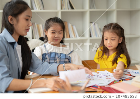Two young Asian girls are enjoying studying English alphabet flashcards with a private teacher Two young Asian girls are enjoying studying English alphabet flashcards with a private teacher 107485658