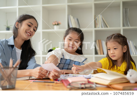 Two adorable Asian girls are focusing on studying English alphabet flashcards with a teacher Two adorable Asian girls are focusing on studying English alphabet flashcards with a teacher 107485659