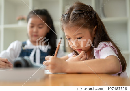 An adorable young Asian elementary school girl is focusing on studying, writing, or drawing 107485728