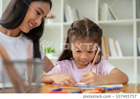 A kind Asian female teacher or babysitter is babysitting and teaching art to a young girl 107485757