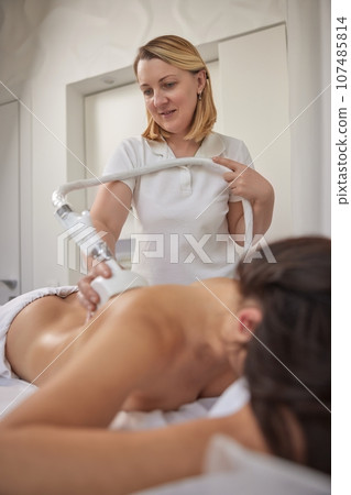 weight loss, Fighting overweight, anti cellulite massage. Young woman is taking part in beauty consultations, body shaping within professional beauty salon, masseur is using vacuum roller massage 107485814