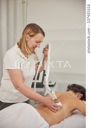 non-invasive method, LPG massage, beauty procedure. Young woman from beauty salon performs beauty services, body shaping, masseurs perform vacuum roller massages for clients, figure correcting 107485816