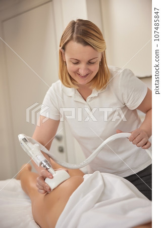 beauty services, anti cellulite, vacuum-roller manipulator. Young woman providing beauty services, body shaping, masseurs performing vacuum roller massage on clients, figure correction, anti-cellulite 107485847