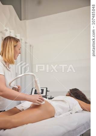 reduce cellulite, roller massage, weight loss. Anti-cellulite massage is being done in professional beauty clinic, and cosmetologist is using roller to massage clients 107485848