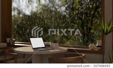 A cozy minimalist cafe or coffee shop on a rainy day, a laptop mockup on a table 107486083