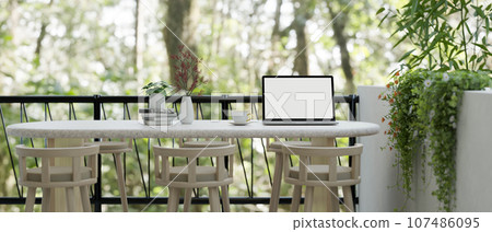 A laptop mockup on a minimal white table on a balcony with a beautiful nature view. 107486095