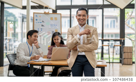 A handsome Asian male CEO stands with a coffee cup in his hand, smiling at the camera A handsome Asian male CEO stands with a coffee cup in his hand, smiling at the camera 107486438