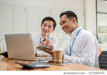 Two cheerful Asian male bankers are looking at a laptop screen and working together Two cheerful Asian male bankers are looking at a laptop screen and working together 107486450