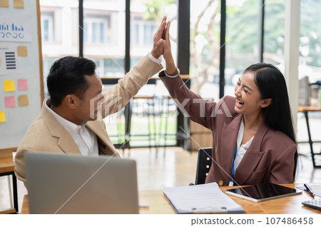 A happy Asian businessman is giving high fives to a female colleague to cheer her up A happy Asian businessman is giving high fives to a female colleague to cheer her up 107486458