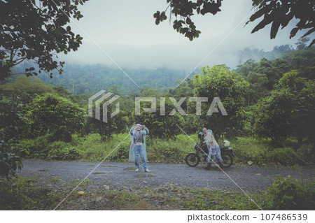 couples of biker pulling small enduro motorcycle on country track among rain falling 107486539