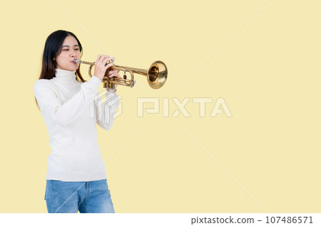 A pretty and talented Asian woman is playing the trumpet, isolated yellow background A pretty and talented Asian woman is playing the trumpet, isolated yellow background 107486571