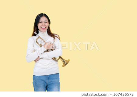 A talented Asian woman is holding the trumpet, an isolated yellow background. 107486572