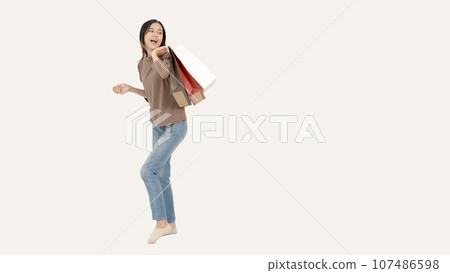 A joyful Asian female with her shopping bags standing against an isolated white background. A joyful Asian female with her shopping bags standing against an isolated white background. 107486598