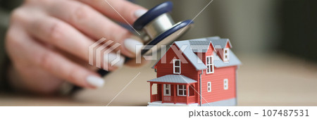 Hand of woman puts stethoscope to house to check condition Hand of woman puts stethoscope to house to check condition 107487531