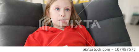 Focused teenage girl in red hoodie holds gaming console Focused teenage girl in red hoodie holds gaming console 107487575