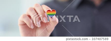 Woman holding small heart with LGBT flag colors closeup 107487589