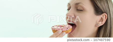 Happy woman bites delicious donut on light background Happy woman bites delicious donut on light background 107487590