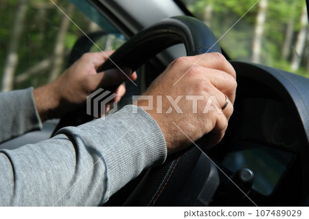 Male Hands holding steering wheel close up. Confident man driving a car during jorney trip. Side view from passenger inside car interior. Summer day. Driver. Selective Focus, Cropped. Travel concept Male Hands holding steering wheel close up. Confident man driving a car during jorney trip. Side view from passenger inside car interior. Summer day. Driver. Selective Focus, Cropped. Travel concept 107489029